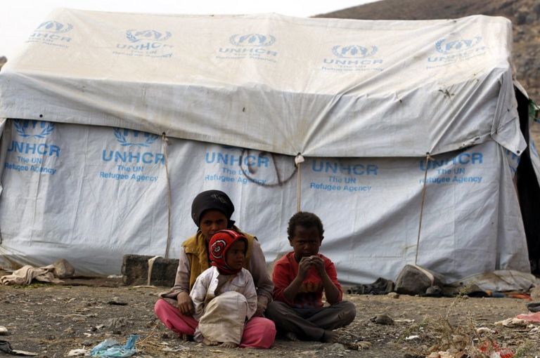 A group of children sit before a UN refugee agency tent