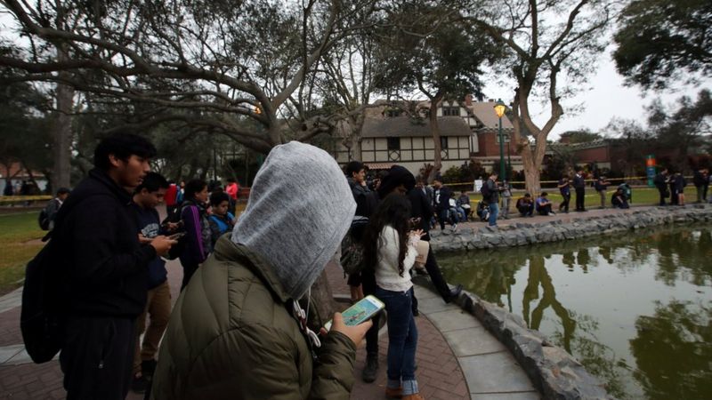 Jovens diante de uma lagoa olhando os celulares