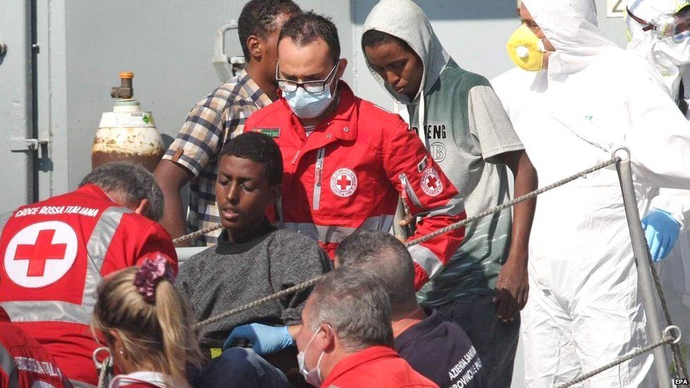 Members of the crew (in white suits) of the Irish Naval vessel the LE Niamh and members of the Italian Red Cross help some 300 migrants as they arrive in Palermo, Italy, on 6 August 2015