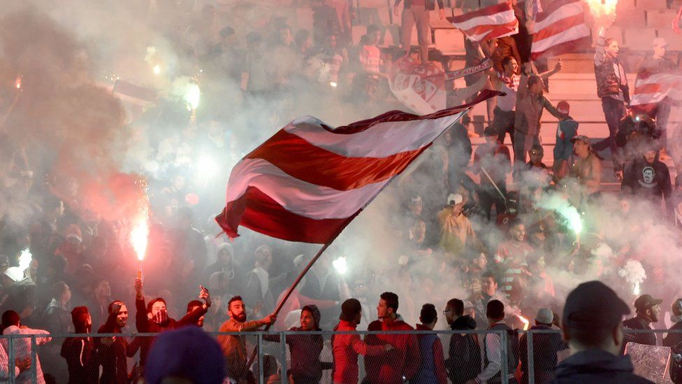 ராடஸ் துறைமுக நகரத்தில் பாரிஸ் செயின்ட்-ஜெர்மெயின் அணியோடு நடைபெற்ற நட்பு விளையாட்டு போட்டியில், துனிஷியாவின் கிளப் ஆப்ரிக்கெயின் அணியின் ஆதரவாளர்கள் கொடிகளை அசைத்து, தீ பந்தம் கொளுத்தி மகிழ்கின்றனர்.