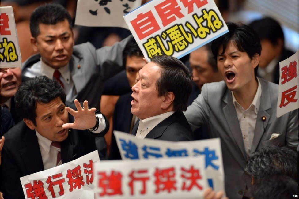 Yasukazu Hamada (C), chairman of a parliamentary panel on Japanese Prime Minister Shinzo Abe's controversial security bills, is surrounded by opposition lawmakers holding placards which say "Opposed to forced passage of the bills", during a parliamentary committee discussion on the bills at the National Diet in Tokyo on 15 July 2015