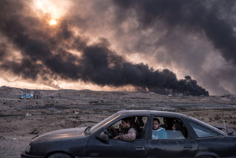 Иракское семейство бежит из Мосула, в котором идут бои, на фоне горящих нефтяных приисков