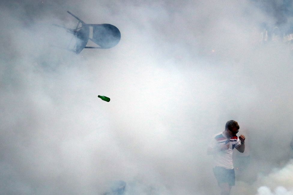 A bottle and chair are thrown as an England fan walks through tear gas as England fans clash with police in Marseille on 10 June 2016.