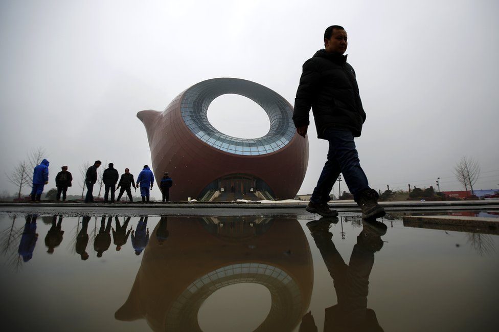Workers stand next to a building shaped like a clay teapot in Wuxi