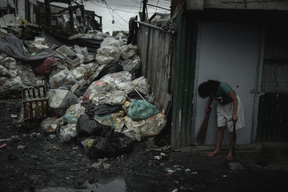 A woman sweeping the front of her house in Happyland a dump site in Tondo, Manila