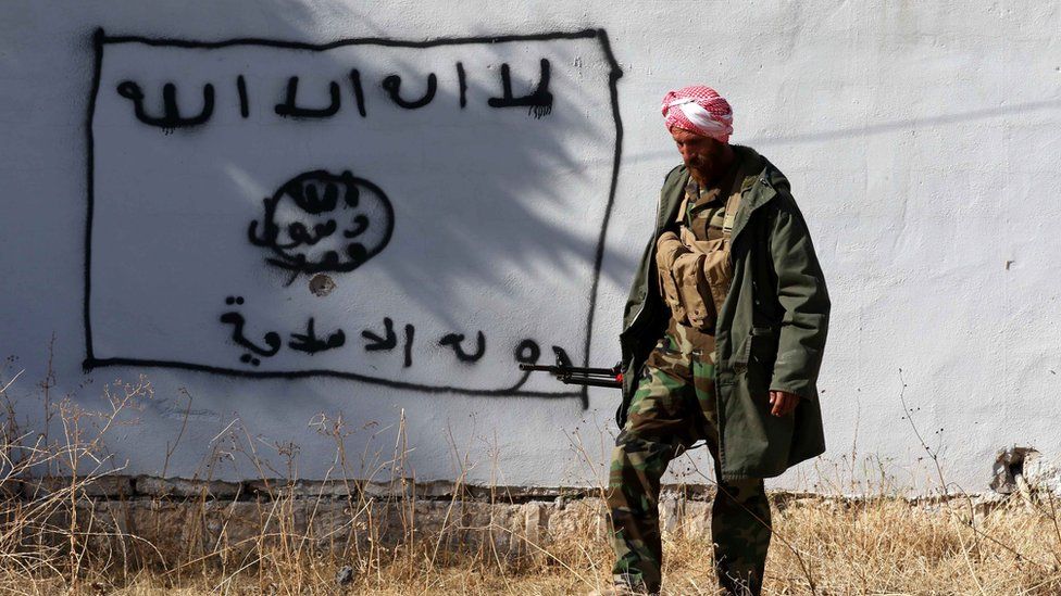 A Kurdish fighter walks by a wall bearing a drawing of the flag of the Islamic State (IS) group in the northern Iraqi town of Sinjar, in the Nineveh Province, on November 13, 2015