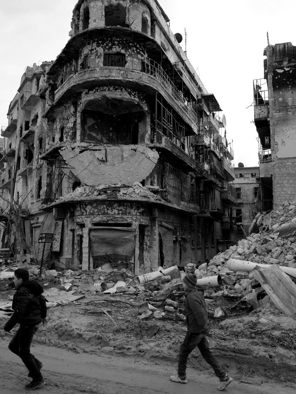 Children walk past war-damaged buildings in Aleppo