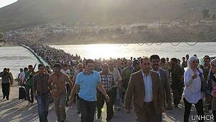 Una multitud de refugiados sirios cruzando un puente.
