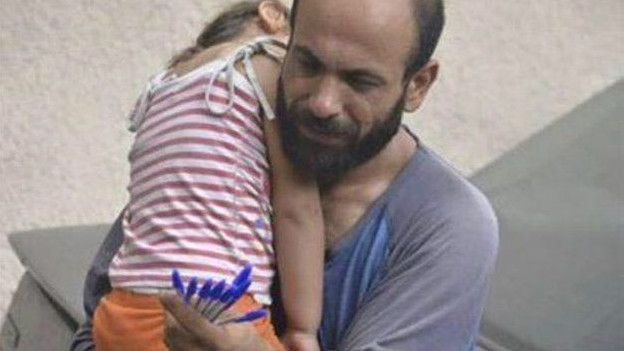 Un inmigrante ofrece en bolígrafos en venta mientras carga a su hija