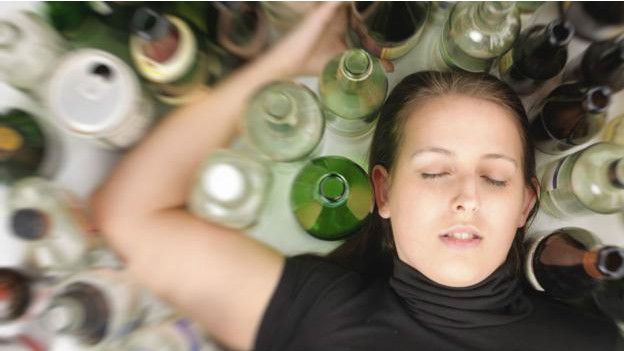 Una persona inconsciente entre muchas copas y vasos