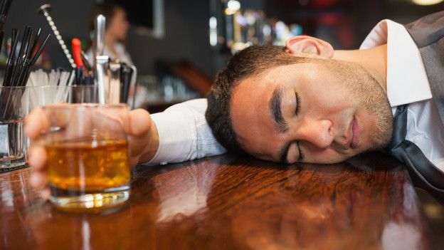 Hombre dormido en mostrador mientras agarra vaso de cerveza