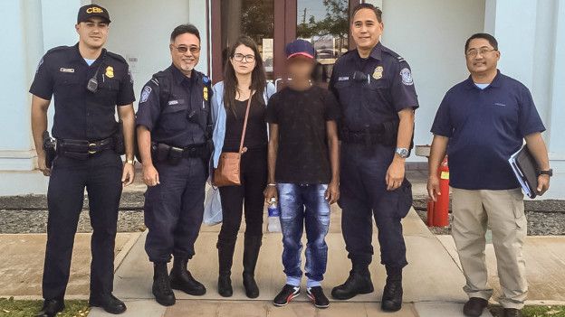 En joven rescatado posa en la foto junto a guardacostas de EE.UU. en Honolulu y con Carolina Ramos, funcionaria de la Cancillería colombiana.