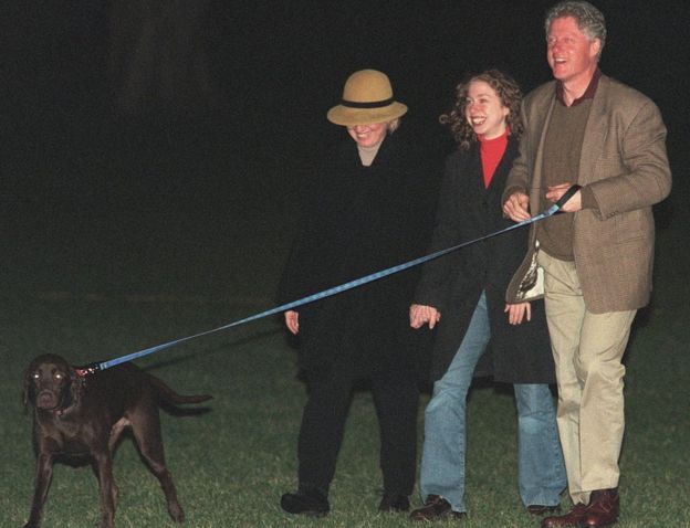 Hillary, Chelsea y Bill Clinton sonrientes con un perro