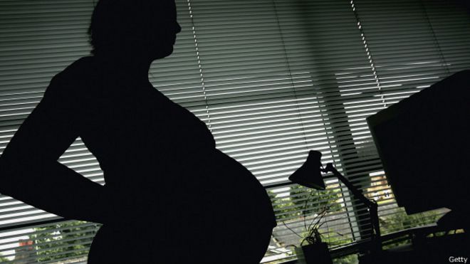Una mujer embarazada delante de una ventana. 