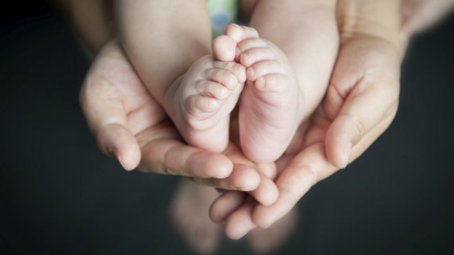 Unos pies de bebé entre las manos de un adulto