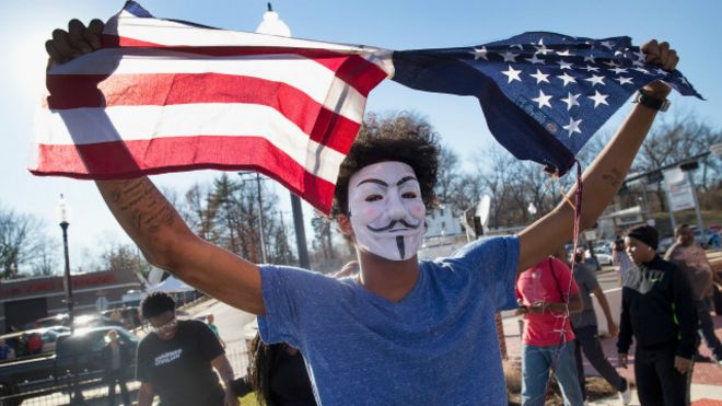 Un joven enmascarado rompiendo una bandera de EEUU