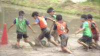 Japanese children play football in a rice paddy