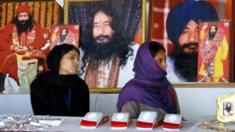 Indian followers of dead guru Ashutosh Maharaj sit in front of posters of him at his ashram on 14 December, 2014