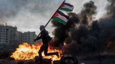 A Palestinian protester runs past a burning barricade carrying a Palestinian flag - 9 December 2017