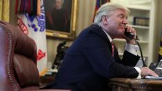 Donald Trump smiles with a corded telephone in his left hand in the Oval office