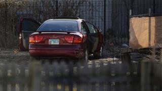 A vehicle riddled with bullet holes sits parked in an alley as Chicago Police Officers investigate a triple shooting on Chicago's West Side.