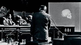 Hombre habla durante un juicio. En una pantalla se exhibe un cráneo.