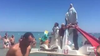 A priest blesses bathers from the back of a seaside pedalo