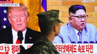 A South Korean soldier walks past a television screen showing pictures of US President Donald Trump (L) and North Korean leader Kim Jong Un