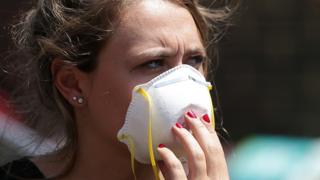A woman wears a mask as she waits near a Grenfell Tower, a residential block of flats in west London on June 14, 2017, as firefighters continue to control a fire that started in the flats in the early hours of the morning.