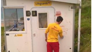 A lifeguard cleans graffiti from a vandalised lifeguard hut