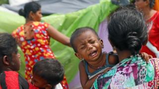 A boy who lives in a temporary shelter cries as his mother walks along a street near a flood affected area in Kelaniya