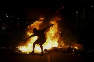 A young man practices a skateboarding move in front of a fire set by protestors following a demonstration against proposed federal government reforms on 15 March 2017 in Rio de Janeiro