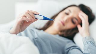 Woman in bed with thermometer (Posed by model)