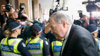 George Pell enters Melbourne Magistrates' Court, shielded from the media by a line of police