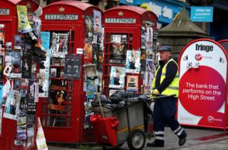 Street cleaner by flyposted phone boxes