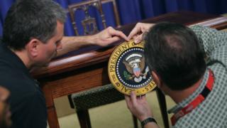 Workers affix the US presidential seal on a desk in the White House