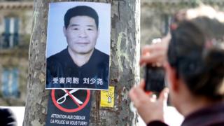 巴黎共和國廣場悼念劉少堯集會現場一名男子朝著貼在樹上的劉少堯遺照拍照(2/4/2017)