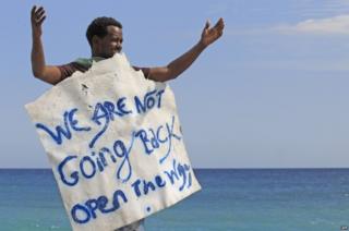 A migrant holds a placard reading "We are not going back" as he waits near the sea, in the city of Ventimiglia at the French-Italian border, on 15 June 2015