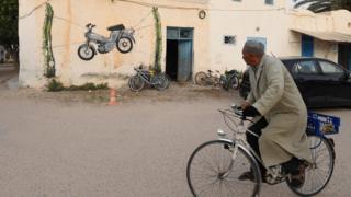 A Tunisian man rides his bike past graffiti in the Tunisian resort island of Djerba on May 1, 2018