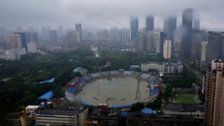 Wuhan - in foreground, flooded stadium, in background, skyscrapers covered in fog