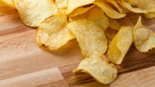 A stock image of crisps (or "potato chips" in some places) spilling across a wooden table.