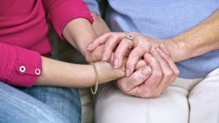 An elderly person holds hand with carer