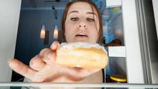 Una mujer toma un pedazo de torta del refrigerador.
