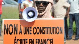 A man carries a megaphone and a banner reading "No to the referendum written in France" during a demonstration against a referendum on a constitutional revision on July 1, 20217, in Bamako.