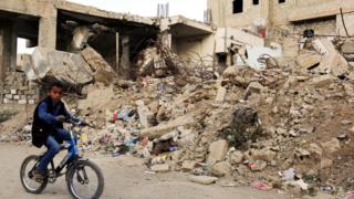 A Yemeni boy cycles past a house destroyed in an air strike in Sanaa, Yemen (21 November 2016)
