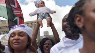 A protester carries a doll as she and others march towards a restaurant after a female client was allegedly thrown out for breastfeeding and not covering up in Nairobi"s Central Business District on May 15, 2018