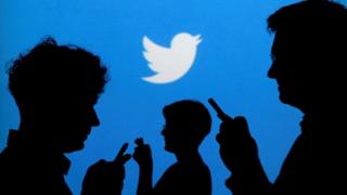 People holding mobile phones are silhouetted against a backdrop projected with the Twitter logo