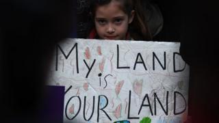 Girl holding sign "my land is our land"