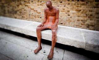 Life-sized sculpture sitting on a concrete bench