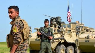 Bir ypg savaşçısı, ABD bayrağı dalgalanan tankın önünde